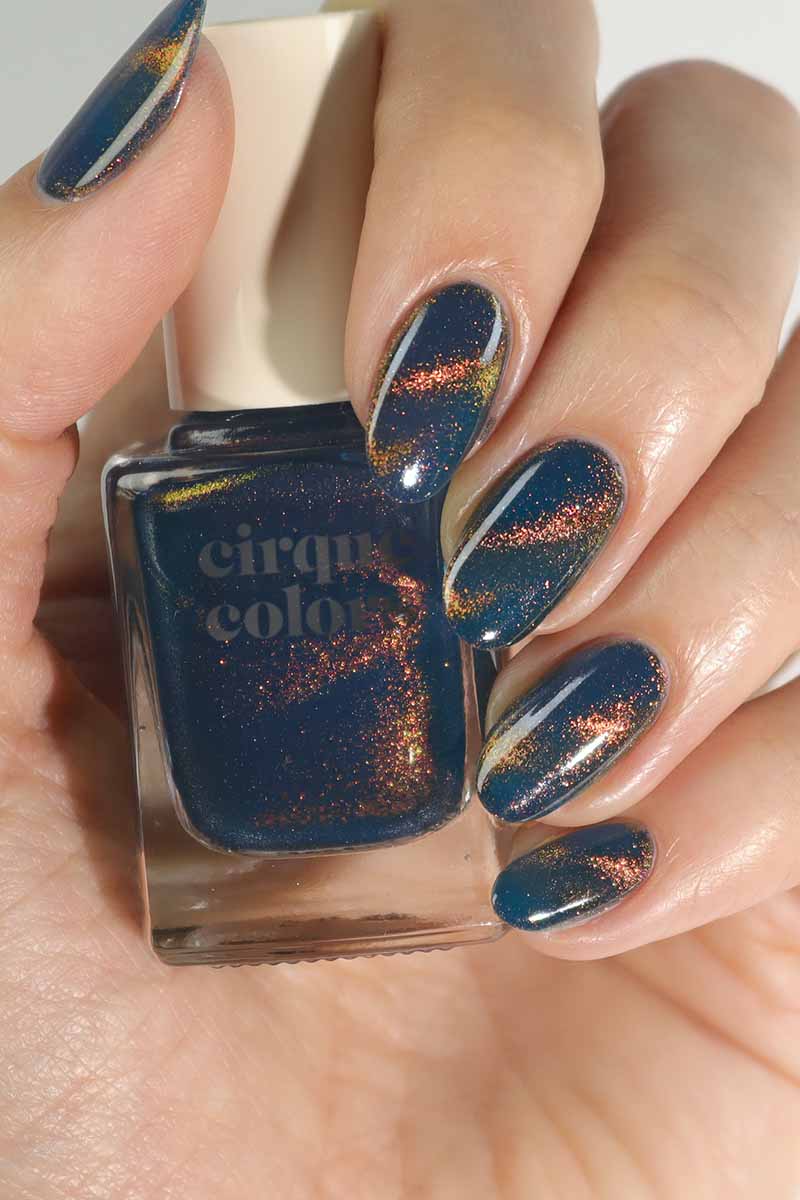 Cirque Colors Castle in the Sky deep sea teal blue nail polish with multichrome magnetic pigment with hand model holding bottle