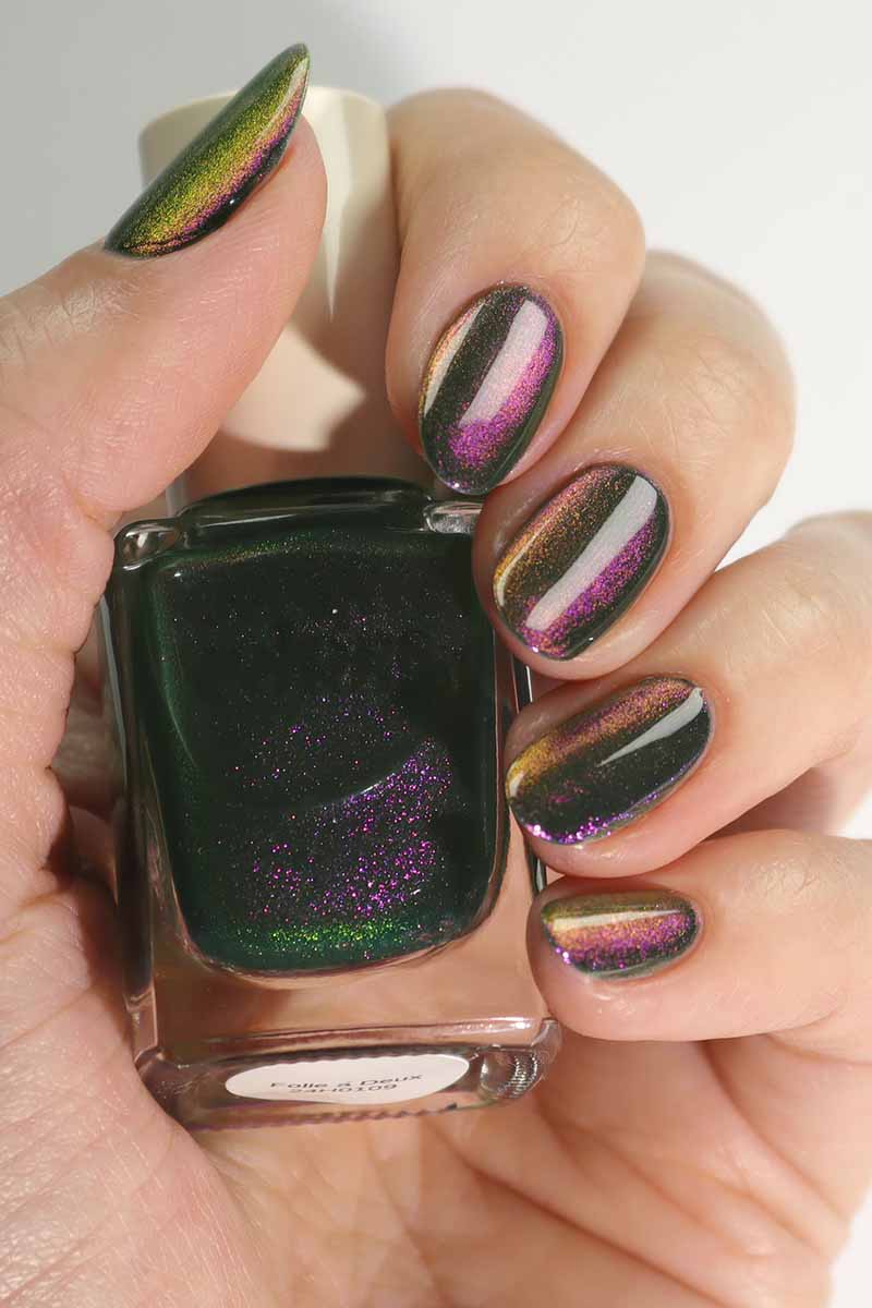 Hand model holding Cirque Colors Folie á Deux bottle, showcasing forest green magnetic nail polish with magenta-green-gold multichrome shimmer on nails