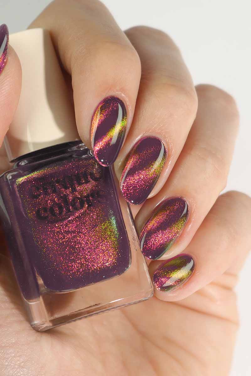 Hand model holding Cirque Colors Fool’s Paradise nail polish bottle with amethyst purple magnetic multichrome polish on nails, featuring rose pink, orange, gold, and green shimmer effects