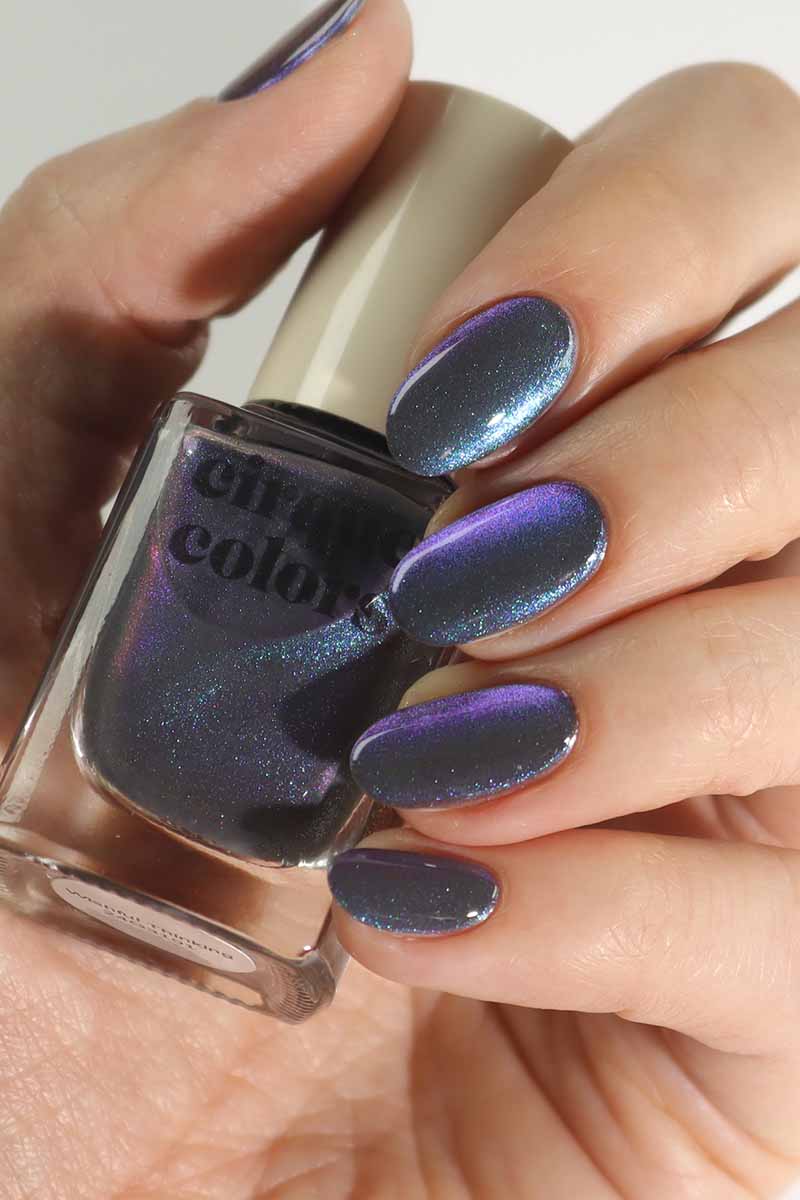 Hand model holding Cirque Colors Wishful Thinking bottle, showcasing smoke-gray magnetic nail polish with aqua-blue-violet multichrome shimmer on nails