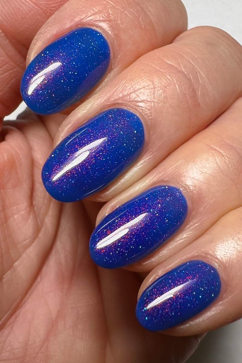 cirque colors cobalt blue shimmer nail polish on hand model close up 